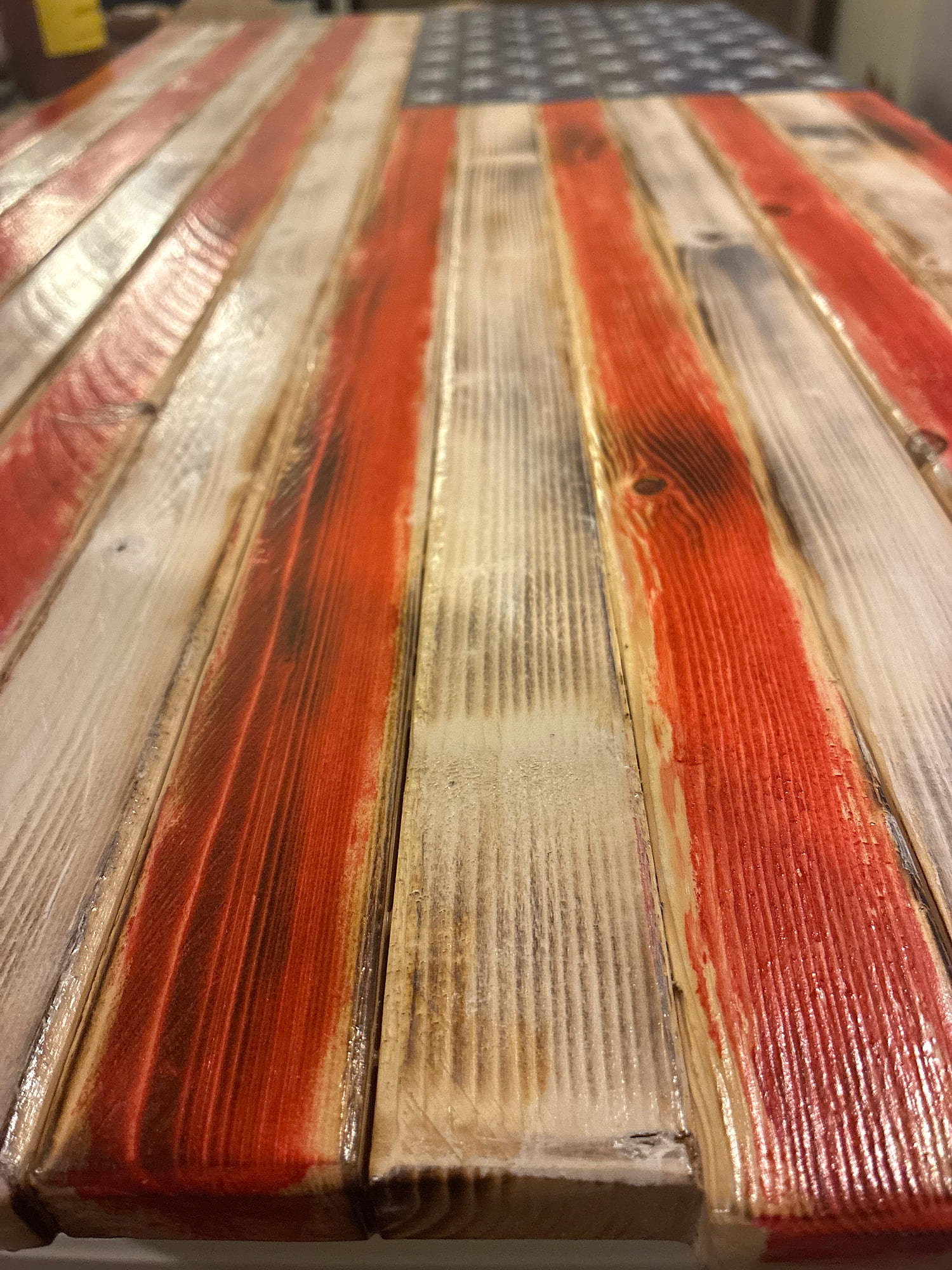 Angled view down the distressed, hand-stained hardwood stripes of a rustic wood American flag toward the stenciled star field