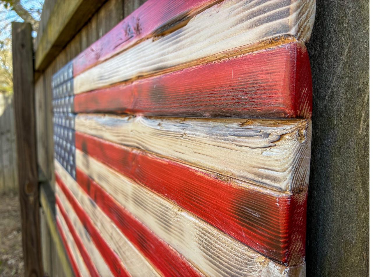 Close-up of a handcrafted wood American flag showing the torch-burned 3D wood grain and hand-stained red and cream stripes — solid pine, made by hand in Trussville, Alabama