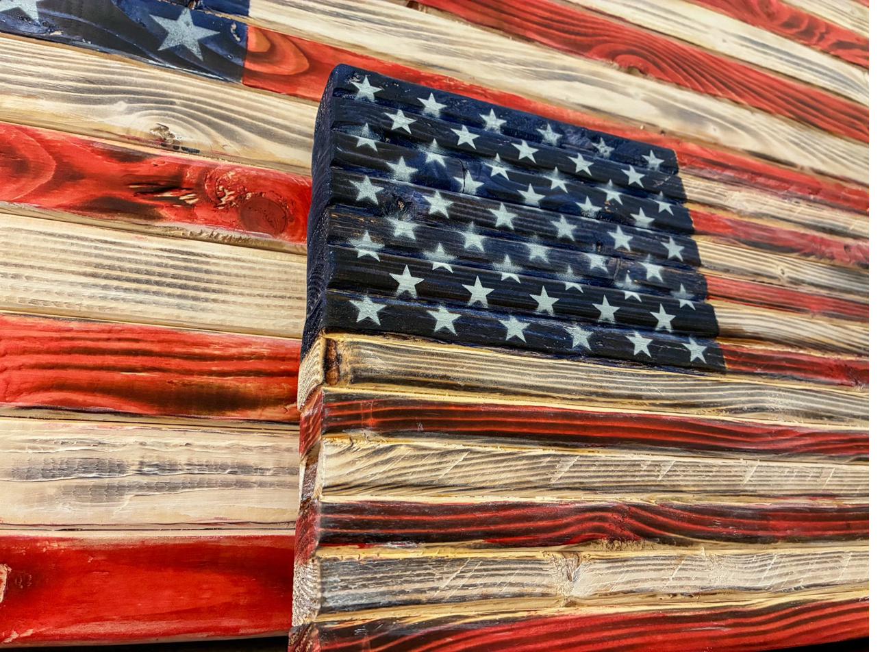Close-up of the stenciled, spray-painted white stars and deep blue field of a rustic wood American flag, showing the charred hardwood grain